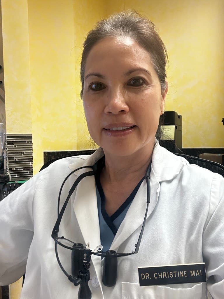 Professional portrait of Dr. Christine Mai wearing a white lab coat and dental loupes.